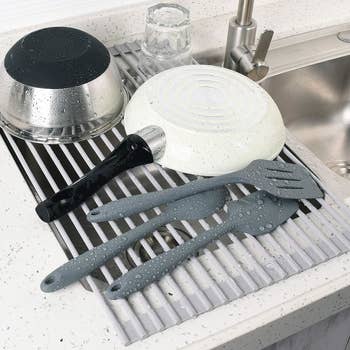 a fry pan, bowl, and utensils drying on roll-up rack over a sink